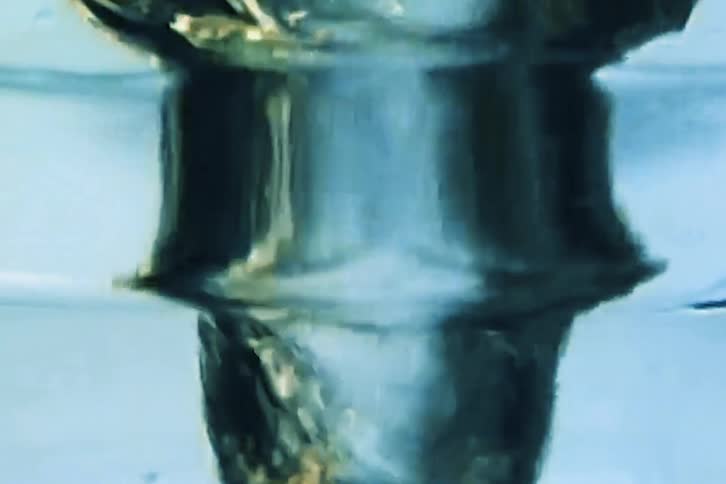 A powerful vortex of water swirling inside a transparent container creating a dark funnellike shape in the centerair bubbles and golden particles are pulled into the rotation highlighting the turbulent movement against the cool blue tones of the li