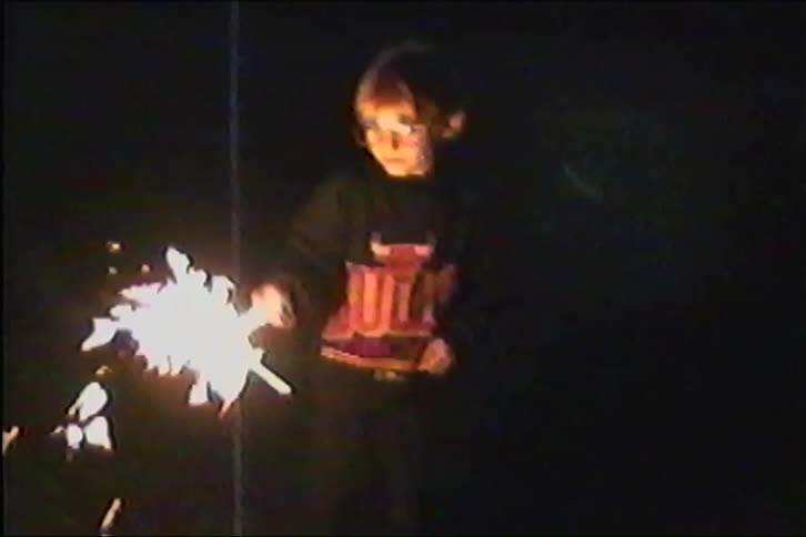 Boy plays with a sparkler while standing in the yard at night