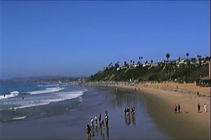 Wide beach with people walking along the wet shoreline and gentle waves in the background