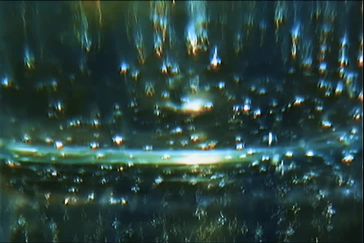 The video shows an abstract highcontrast shot of sparkling lights and bubbles moving within a dark liquidlike environment a distorted horizontal glow stretches across the center of the frame creating a shimmering effect reminiscent of retro film or