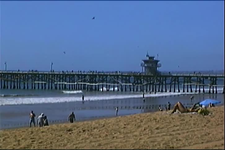 Beach with people on the sand and a pier extending over the ocean in the background