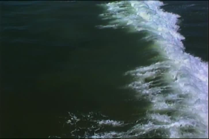 A diagonal line of white churning surf cuts through dark green water capturing a breaking wave midmotion as foam trails and dissipates across the surface