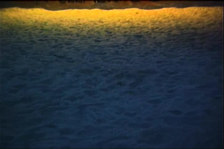 Is is the primary horizontal boundary at the top of the frame where the textured ground meets a bright goldenorange light source it creates a sharp contrast between the dark blue terrain and the warm glow above