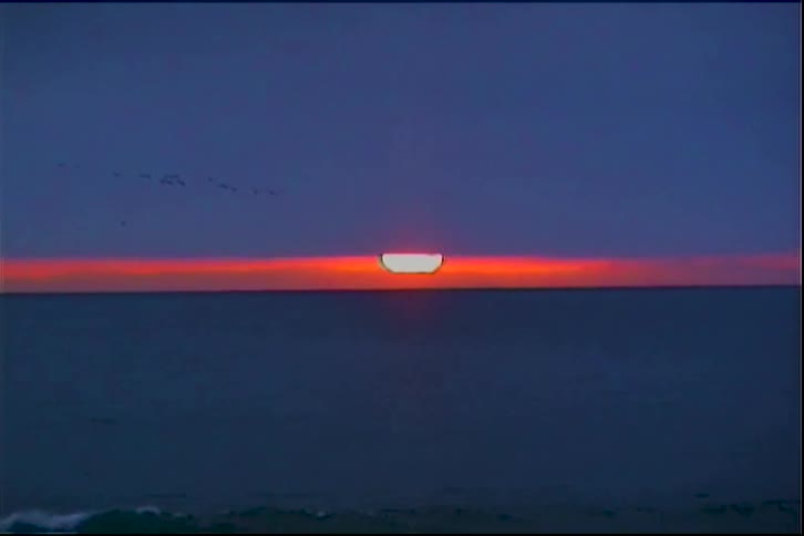 Strip of sunset light on the horizon over the sea with waves breaking on the beach under a cloudy sky
