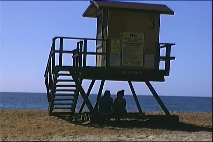 Lifeguard tower elevated above the sand with two people seated in the shade