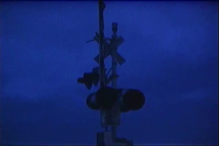 Two vertical beams of light streaks appear during the flickering of a railroad crossing signalone line is a bright blue streak that descends vertically through the center of the frame while another redtinted line appears on the left side as the cross