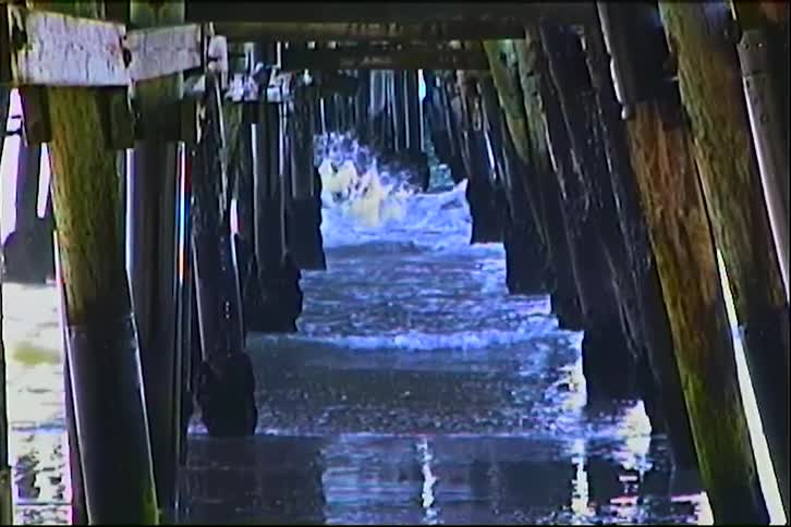 Ocean waves move between wooden pillars beneath a pier