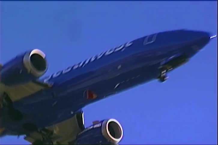 A blue and gold airplane flies directly overhead against a clear blue sky as it prepares to land against a deep blue sky