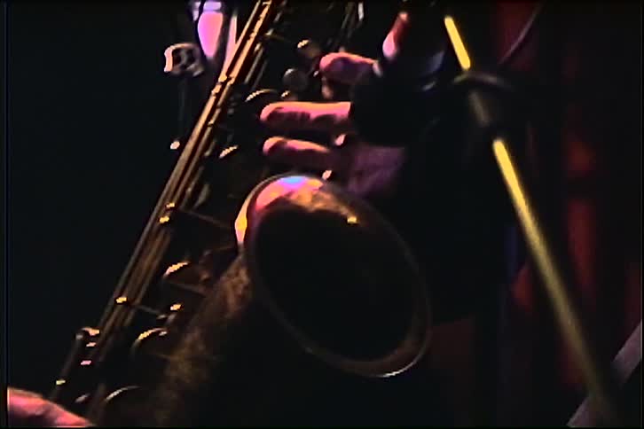 A man in a suit plays a saxophone on a stage with red curtains in the background
