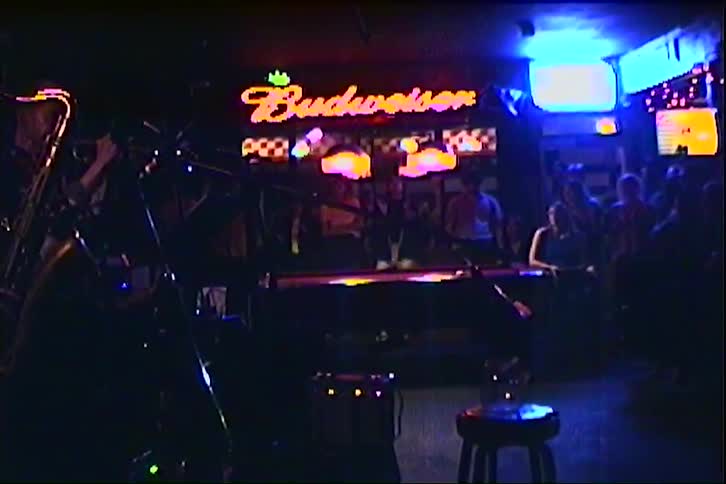 Musician plays saxophone in bar with neon sign in background