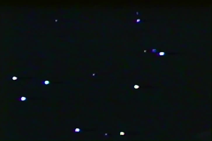 This video features a dark grainy background reminiscent of vintage vhs tapes scattered with flickering white and blue points of light these lights drift across the frame creating a lofi abstract celestial or bokehstyle effect