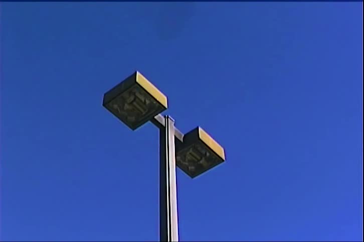 A lowangle shot shows a large commercial airplane flying directly over a doubleheaded street light against a clear blue sky