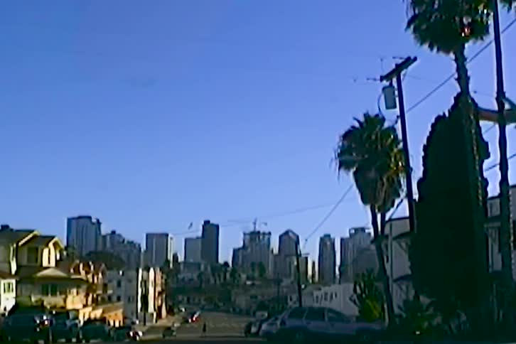 Airplane flying low over an urban area with buildings in the background palm trees and power lines in the foreground