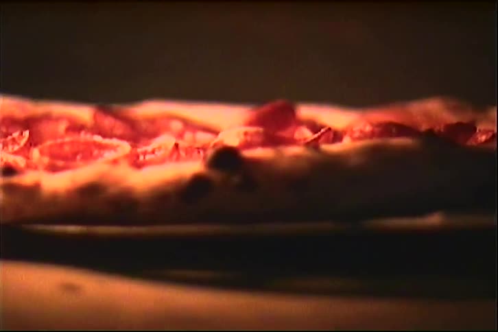 Pepperoni sizzles on a pizza cooking in a pizza oven as it is turned