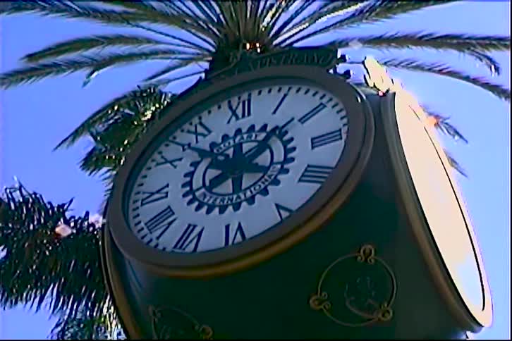 A clock atop a post is located near some palm trees outdoors