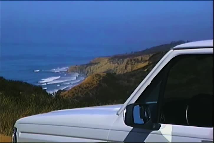 White pickup truck parked on a dirt road overlooking cliffs and the ocean in the background under a blue sky