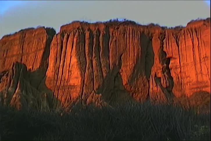 A mountain canyon stretches through the wilderness at sunset with soft grasses covering the canyon floor as warm golden light spills across the rugged cliffs
