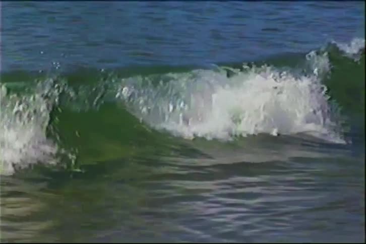 The video shows a wave gradually building and then breaking as it reaches a shoreline the footage has a vintage lowresolution aesthetic characterized by visible scan lines and color distortion