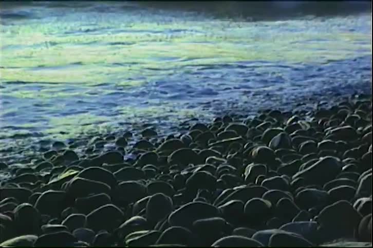 Waves crashing over dark rocks at dusk on ocean coast with warmtoned sky