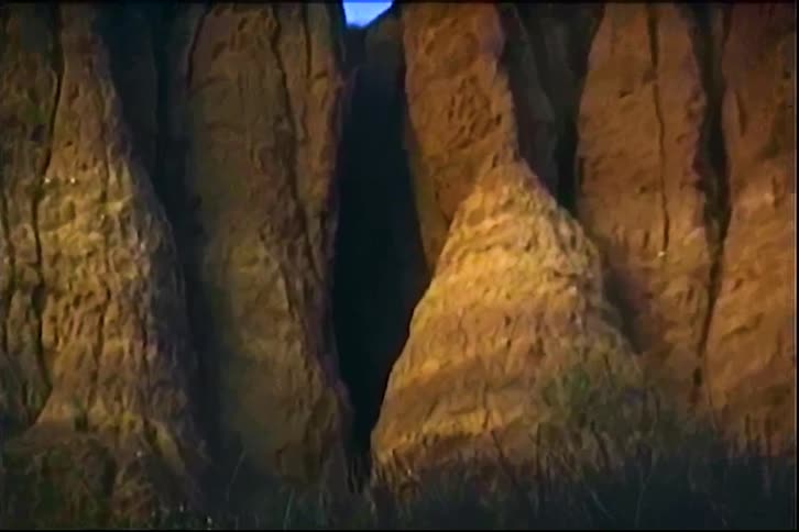Huge rock cliffs surrounding a dark cave entrance outdoors during daytime