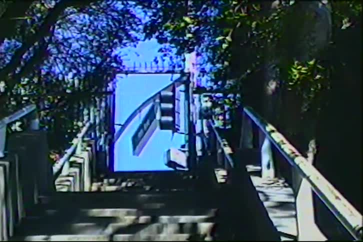Shaded stairway through trees leads to blue structure with transport icon under filtered light