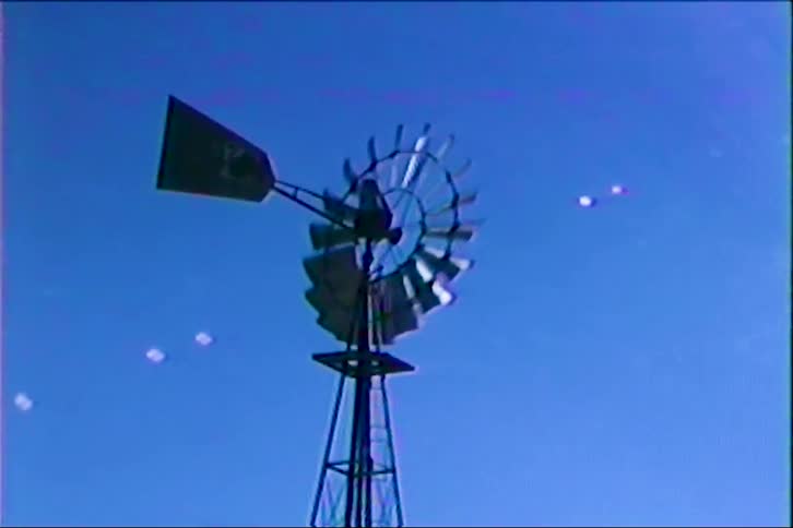 Traditional windmill stands out against blue sky with light flares in the background