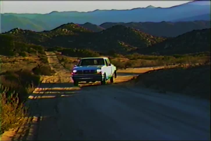White pickup truck on dirt road through dry terrain and mountains under golden morning light