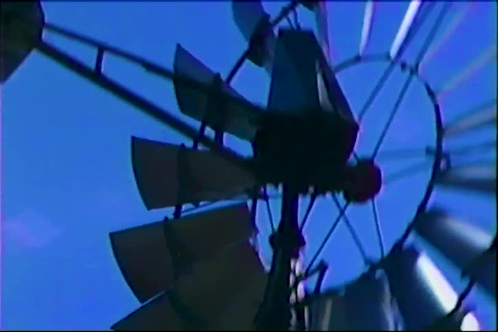 Metal windmill wheel with blades rotates against a blue sky
