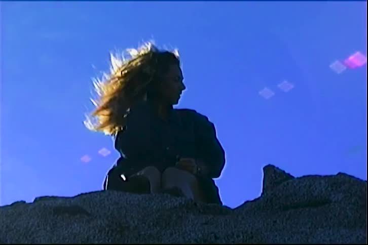 Person sitting on rocks with arms raised under blue sky
