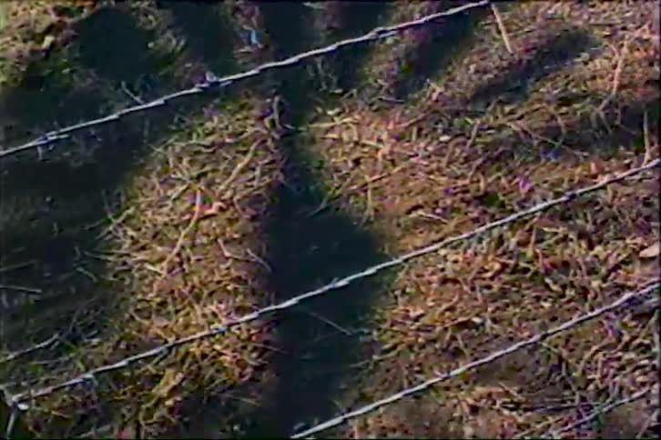 Sunlight reflects across the countryside ground as the fastspinning windmill casts a shifting moving shadow on the floor with a series of barbedwire fences stretching across the surface and cutting through the bright midday light