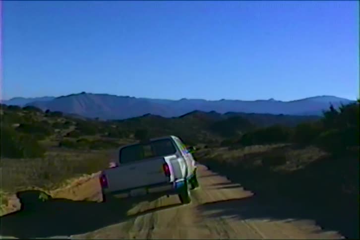 White pickup truck on dirt road surrounded by dry vegetation and mountains in the background