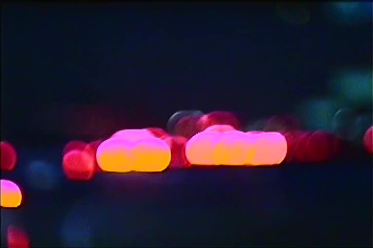 Soft out of focus orbs of red orange and blue light from passing traffic float and drift across the screen against a dark background