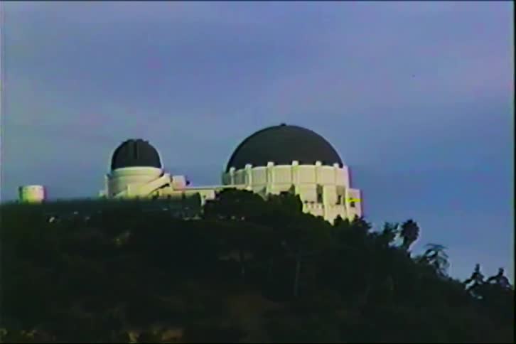 Astronomical observatory with white domes positioned atop a treecovered hill under a blue sky