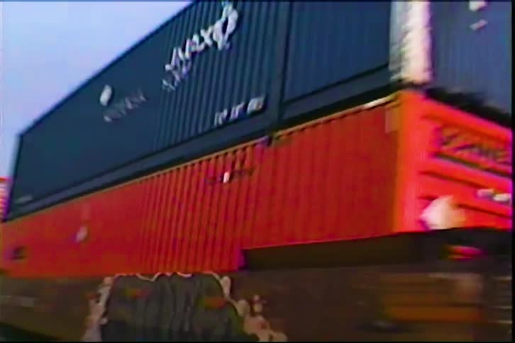 A cargo train passes by at midday carrying a series of containers across the countryside