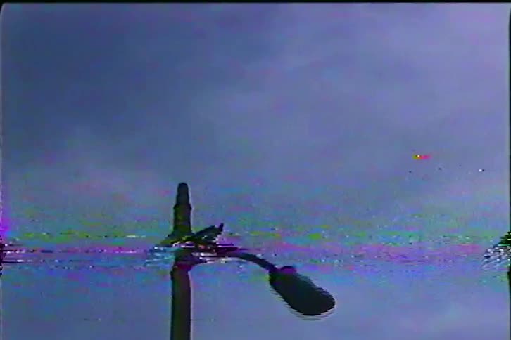 Streetlight pole seen from below against a cloudy sky with visual interference