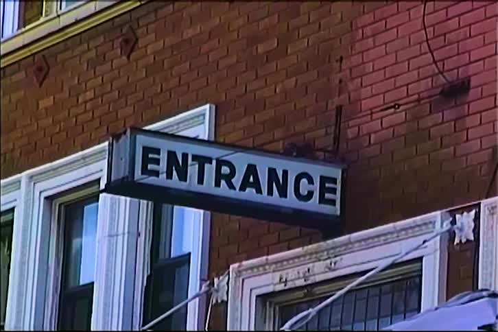 Brick building facade with aligned windows and an entrance sign extending from the wall