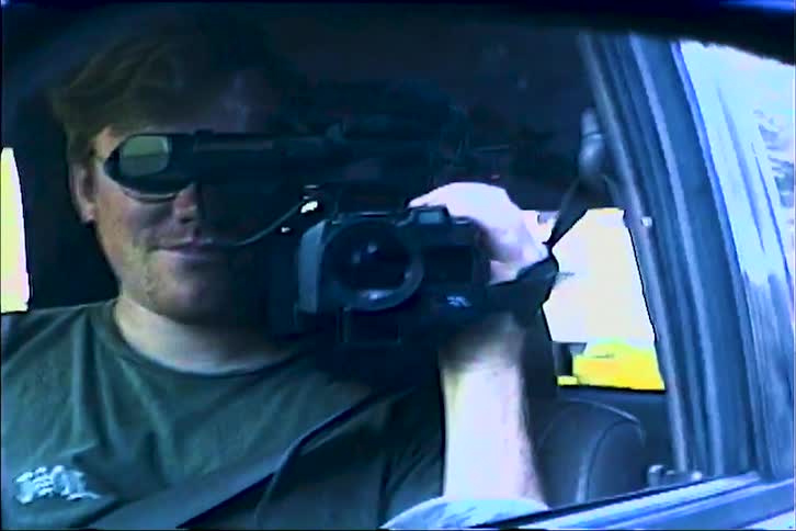 Reflection of a videographer filming through a cars side rearview mirror while in motion