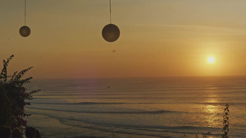 Hanging lamps and foliage framing sunset over the sea