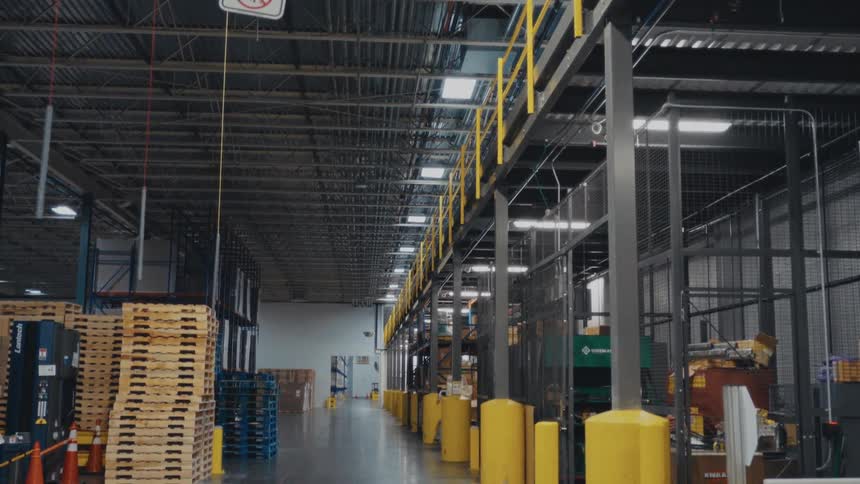 Brightly lit industrial warehouse interior with stacked wooden pallets and safety bollards