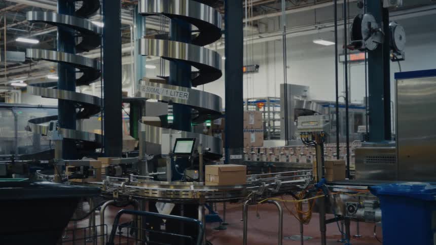 An automated factory conveyor transports cardboard boxes through a modern industrial facility