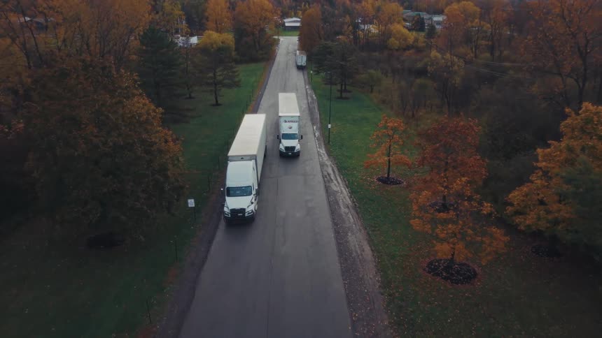 Shipping trucks stopped on a road as one truck passes them