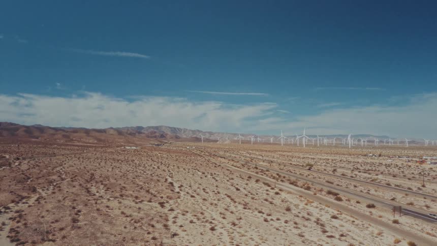 Light traffic moves across the rural desert with a wind farm of turbines spinning in the distance