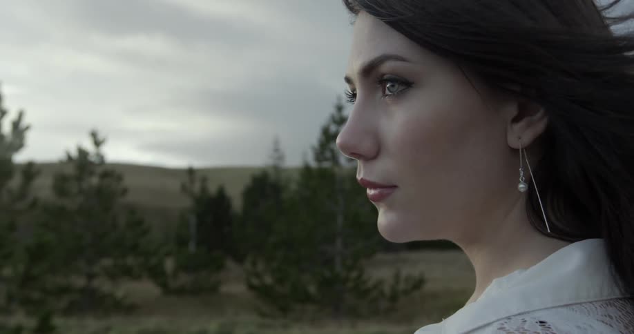 Woman looks out at trees on a cloudy day