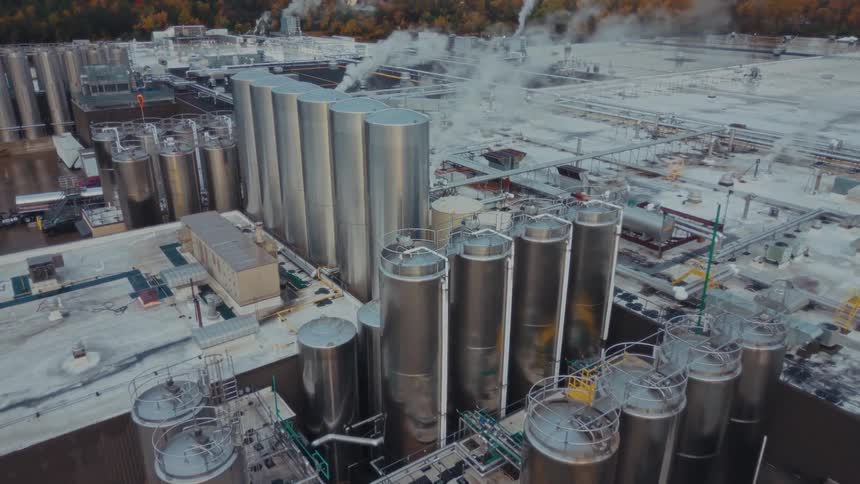 Industrial complex with metal tanks piping and visible steam seen from an aerial perspective
