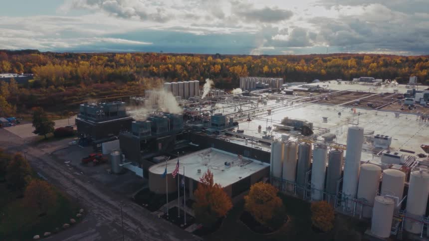 Industrial complex with tanks pipelines and steam emissions surrounded by autumncolored vegetation