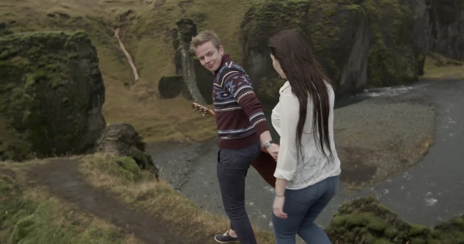 A man holding a guitar leads a woman down a hillside