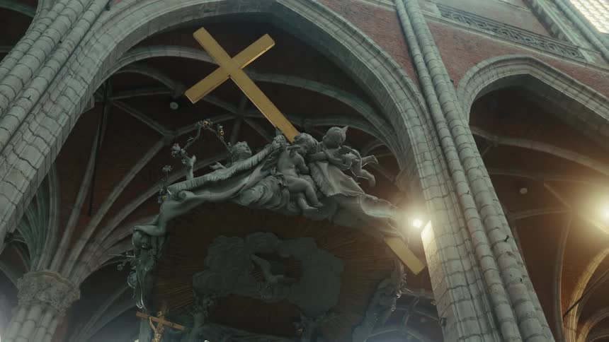 Cherubs hold a gold cross in a statue located near a religious building with arches during the daytime