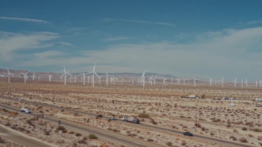 Wind turbines spread across desert with highway and mountains in the background