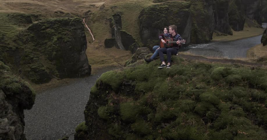 A couple sit on the edge of a small cliff