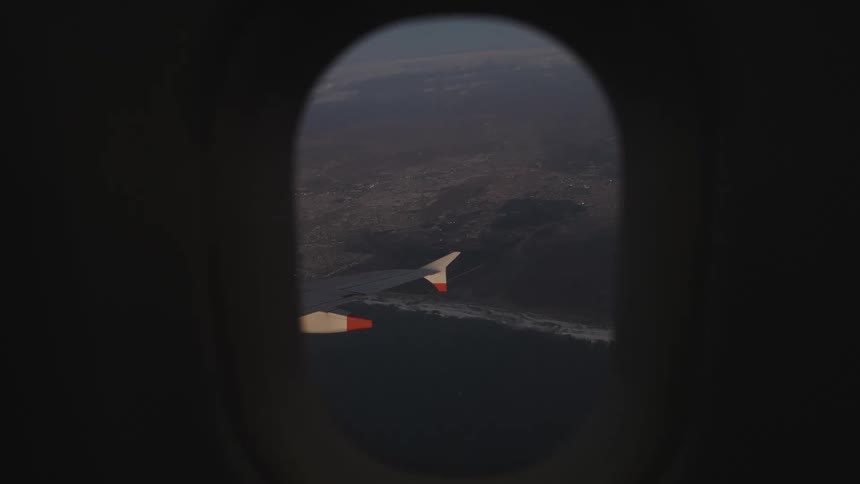 Airplane wing seen through a window with coastline and ocean below at high altitude